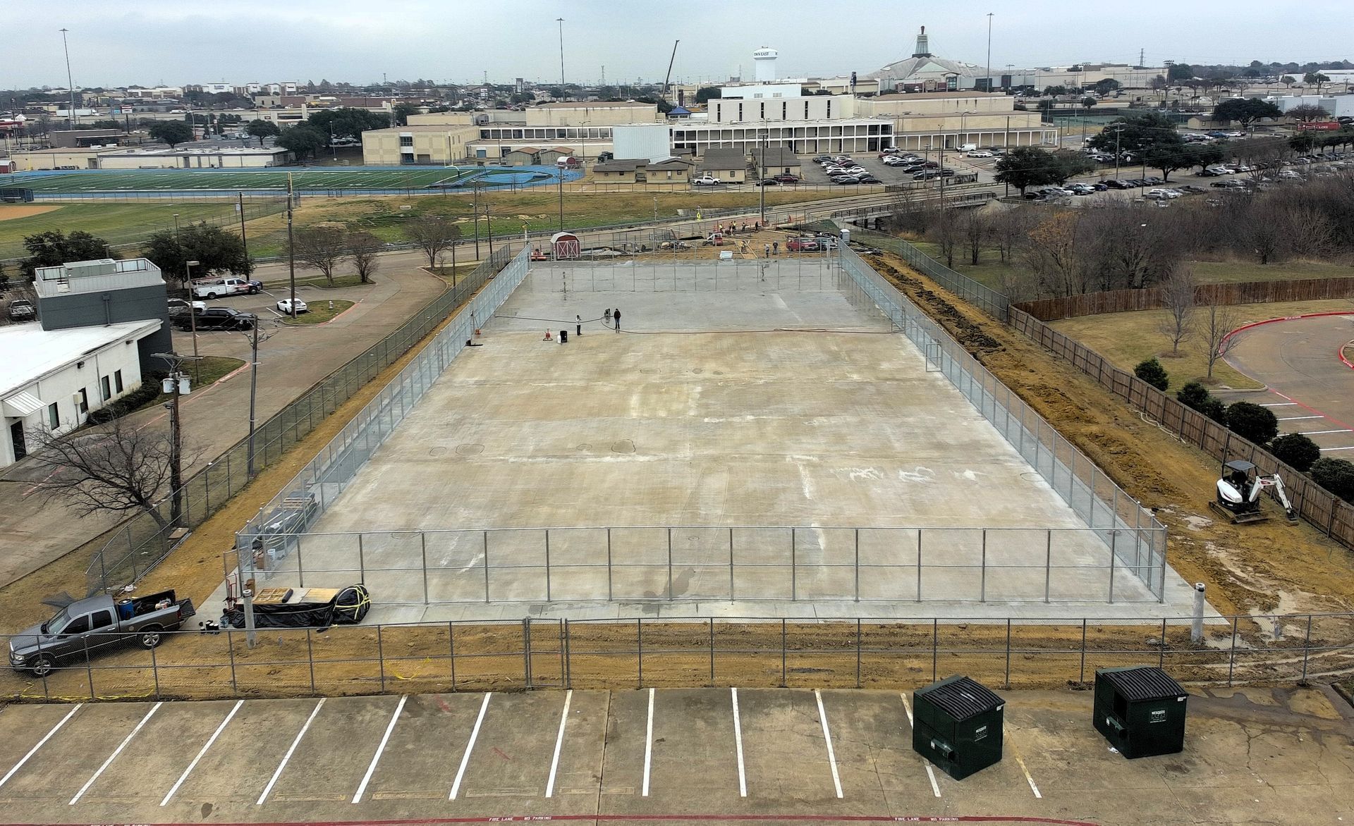 Concrete slab enclosed by a chain-link fence, with nearby buildings and a parking lot.