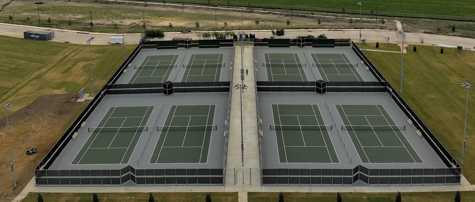 Aerial view of a large outdoor tennis complex with four green courts and a central walkway