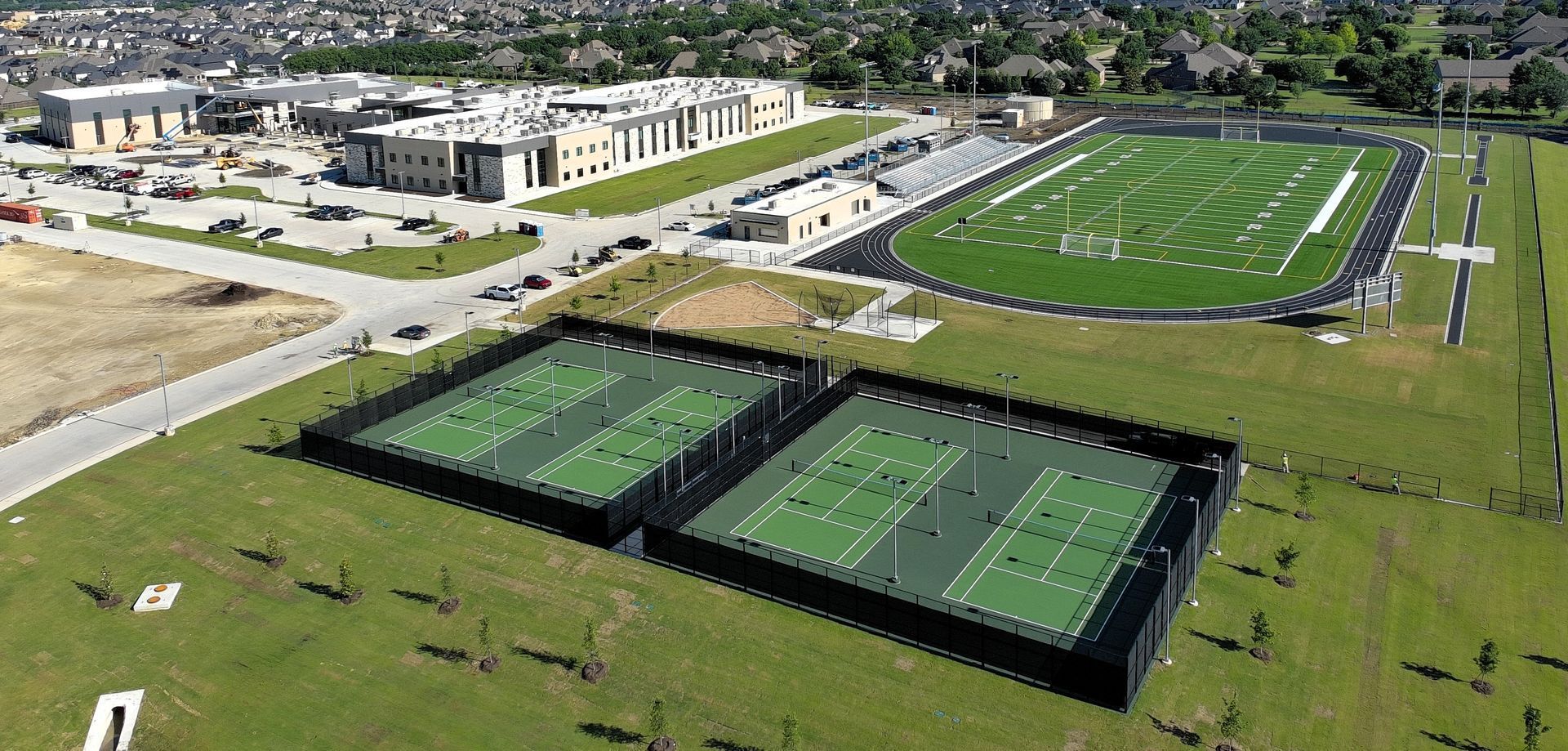 Aerial view of a sports complex with tennis courts, a soccer field, and nearby buildings
