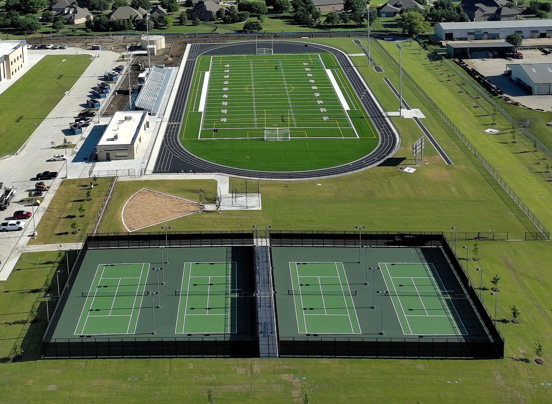 Aerial view of a sports complex with a football field and four fenced tennis courts