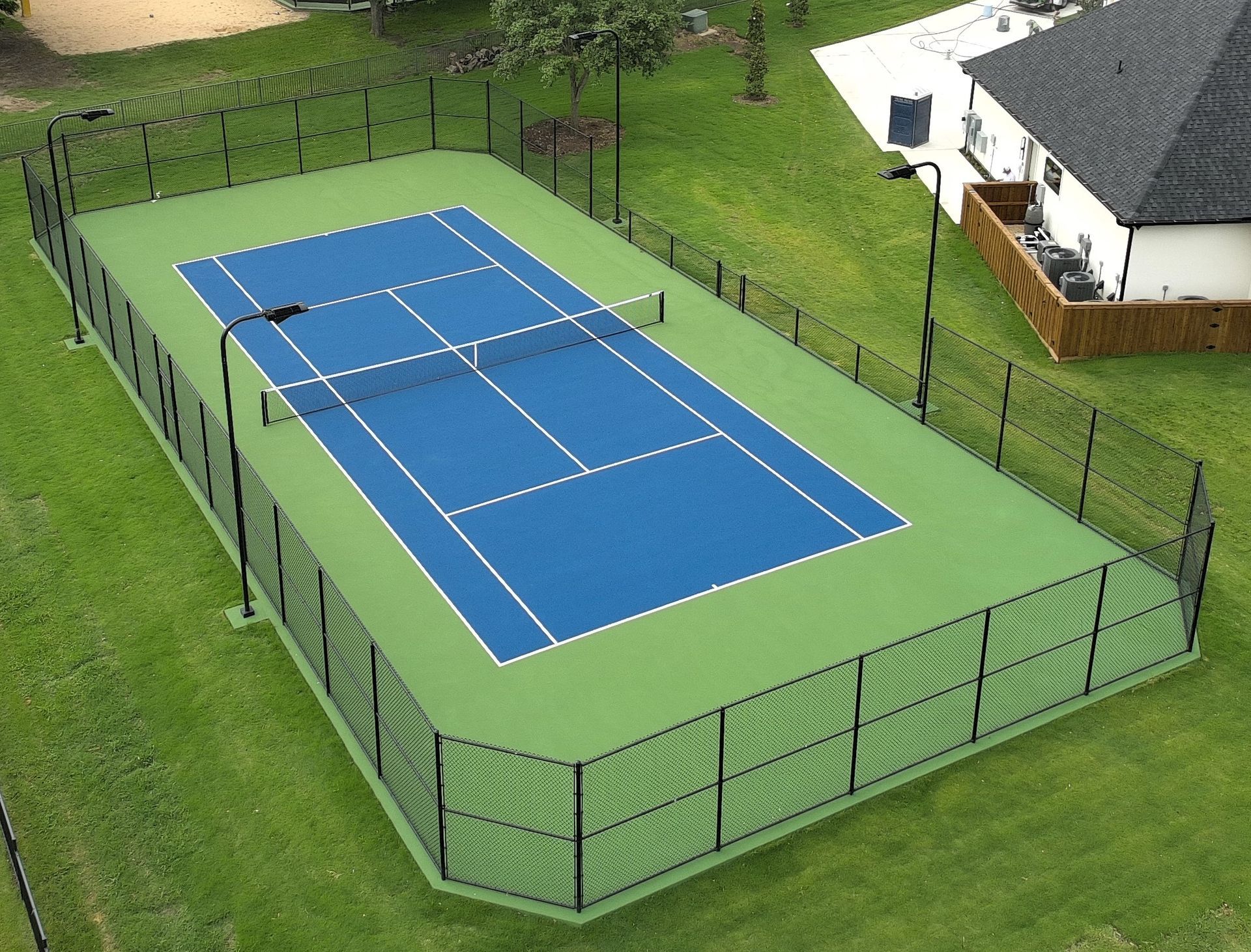 Outdoor fenced blue and green tennis court beside a house, viewed from above