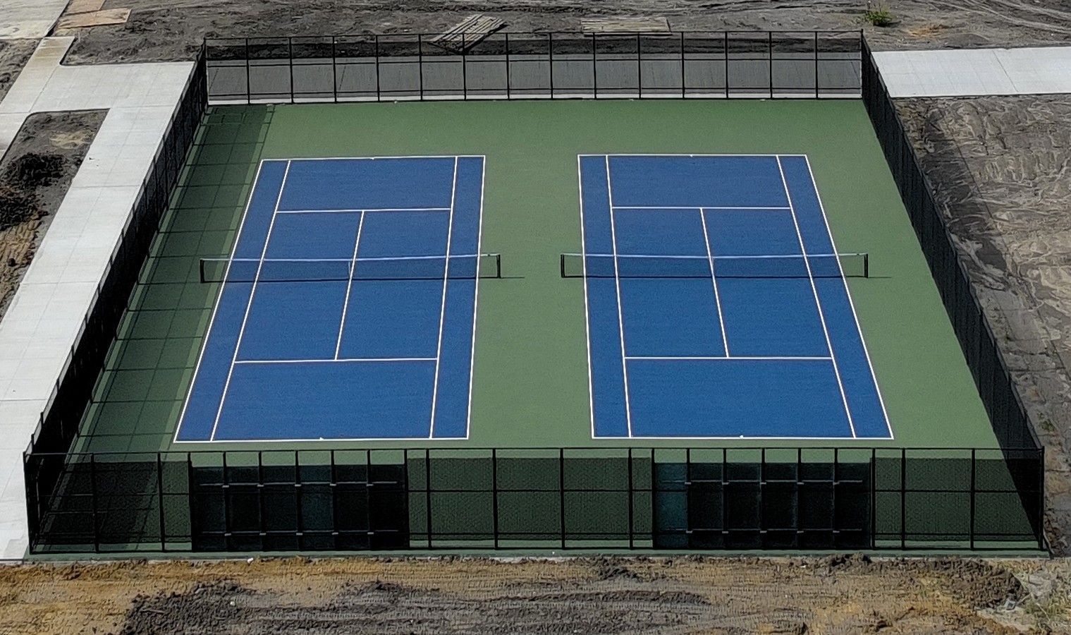 Aerial view of two blue tennis courts enclosed by a green fence on a rooftop.