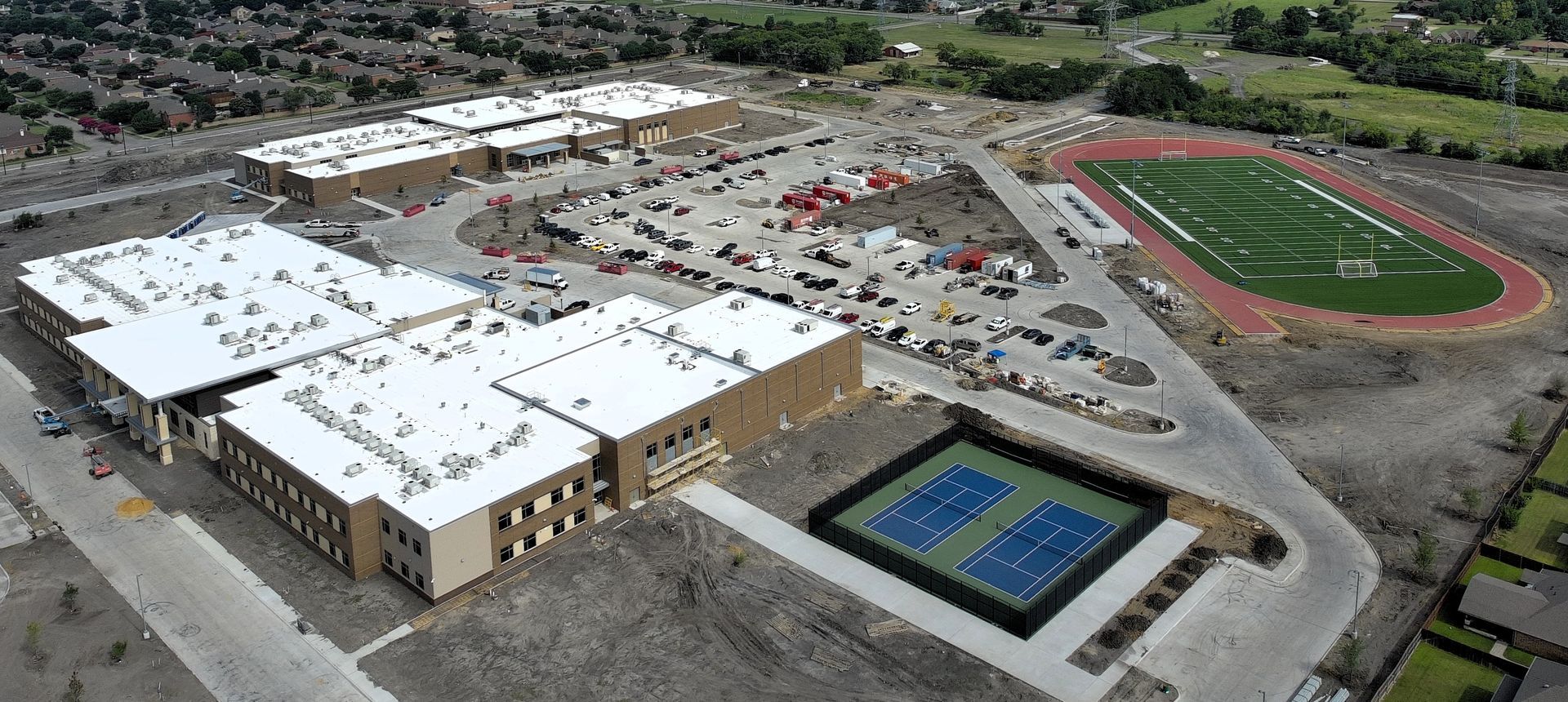 Aerial view of a school campus with buildings, parking lot, tennis courts, and a football field