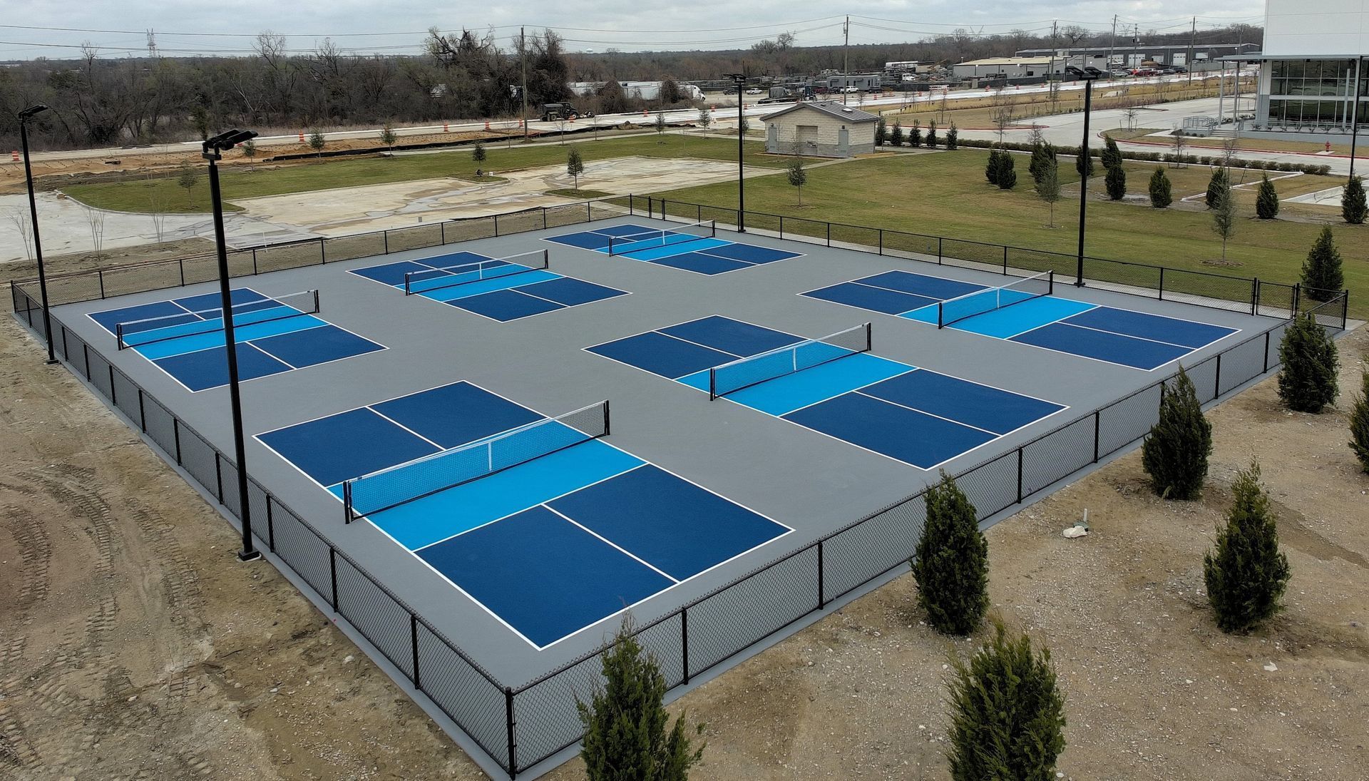 Aerial view of an outdoor pickleball complex with multiple blue courts and gray fencing.