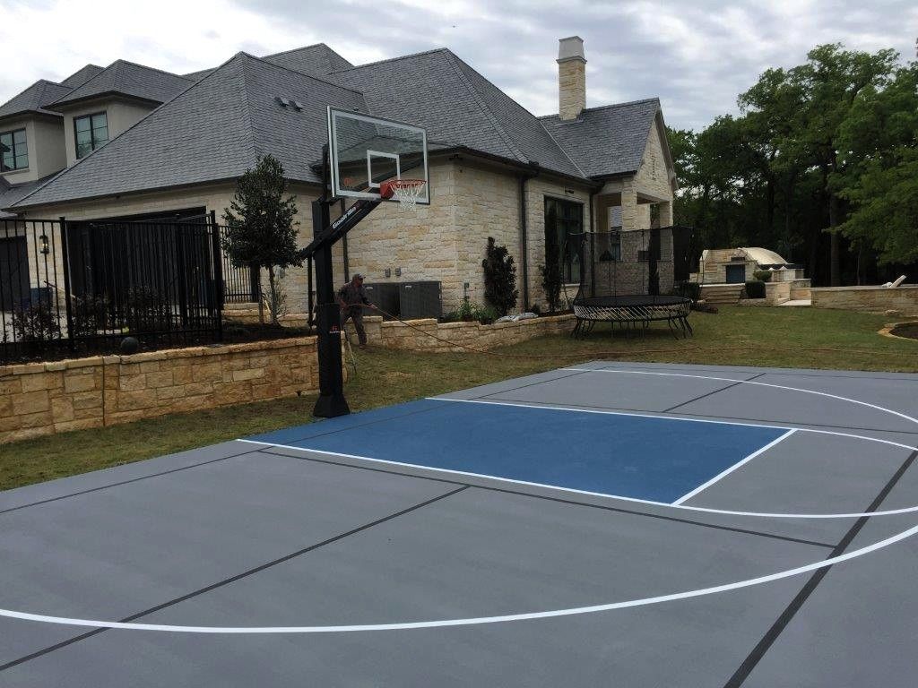 Outdoor basketball court with a hoop beside a stone house and grassy yard