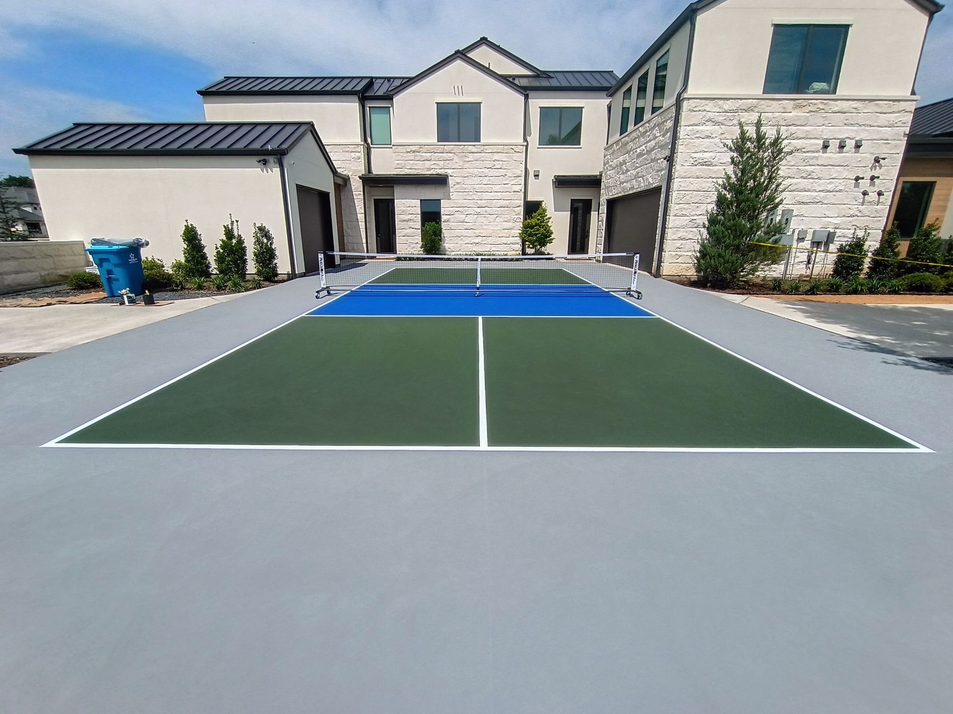 Backyard pickleball court with a blue and green playing surface in front of a modern house