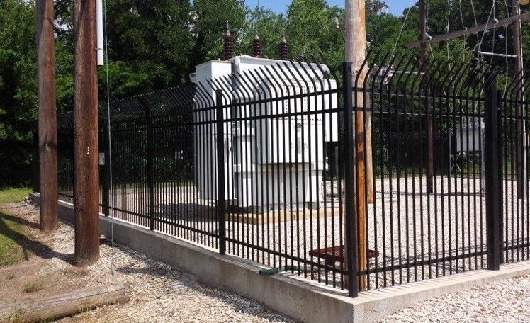 Black security fence surrounding an electrical substation with tall wooden poles.