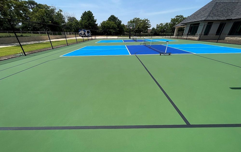 Outdoor pickleball court with green and blue surfaces, net, and building in the background.