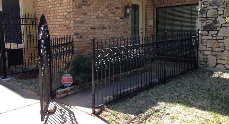 Black wrought-iron ramp and fence leading to a brick and stone building entrance. Security system sign visible.