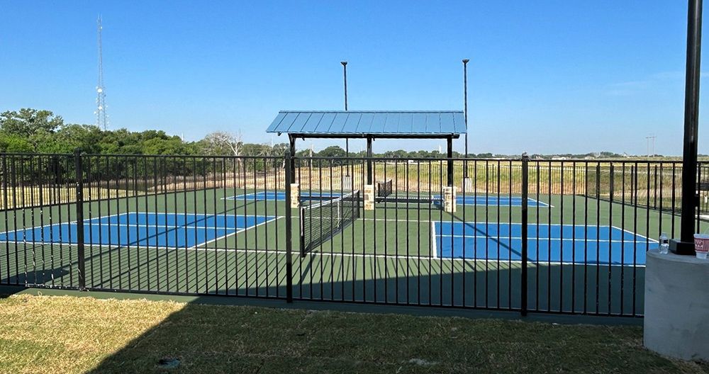 Black fenced-in pickleball courts with a blue roofed shelter on a sunny day.