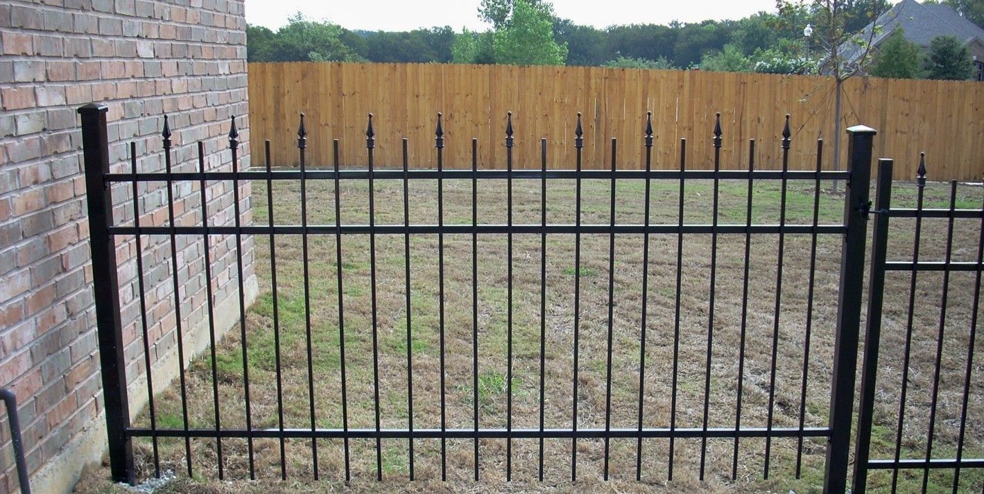 Black metal fence in front of a brick wall and a wooden fence.