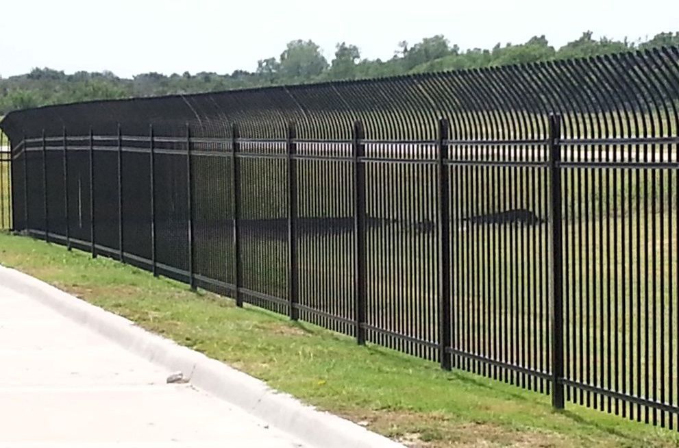 Black metal security fence with curved top, protecting grassy area.