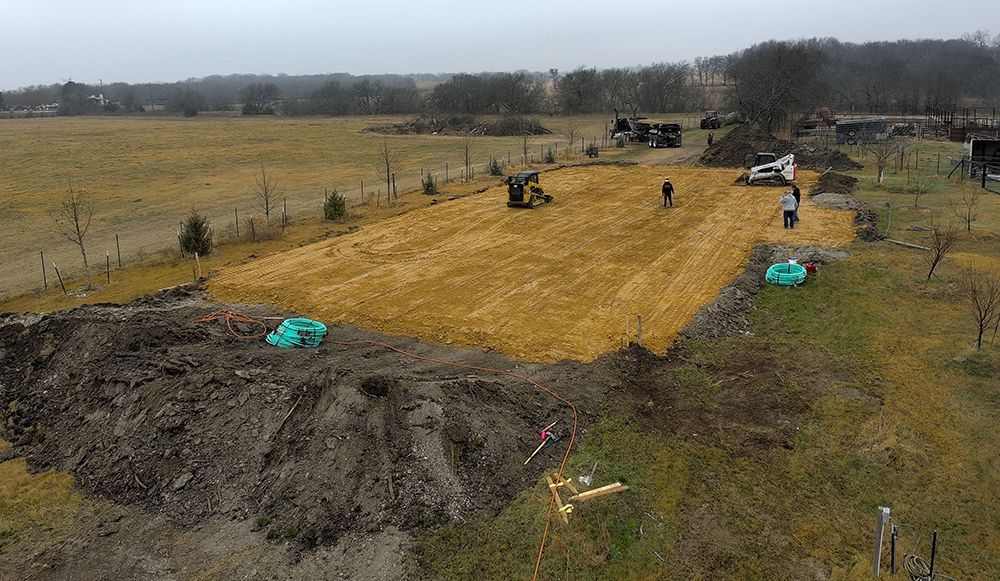 Construction site with dirt fill and two excavators, three workers, and equipment in a field.