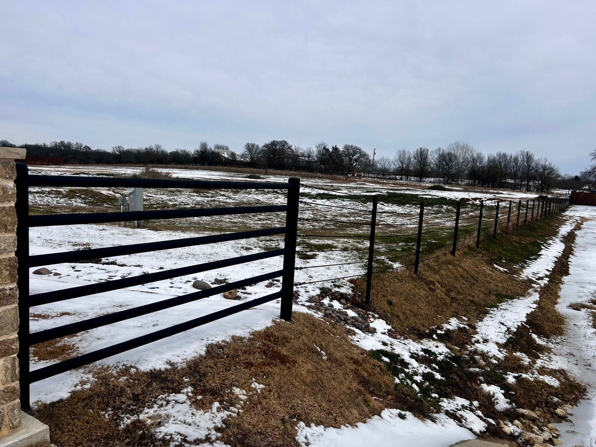 Black metal fence with gate in snowy field.