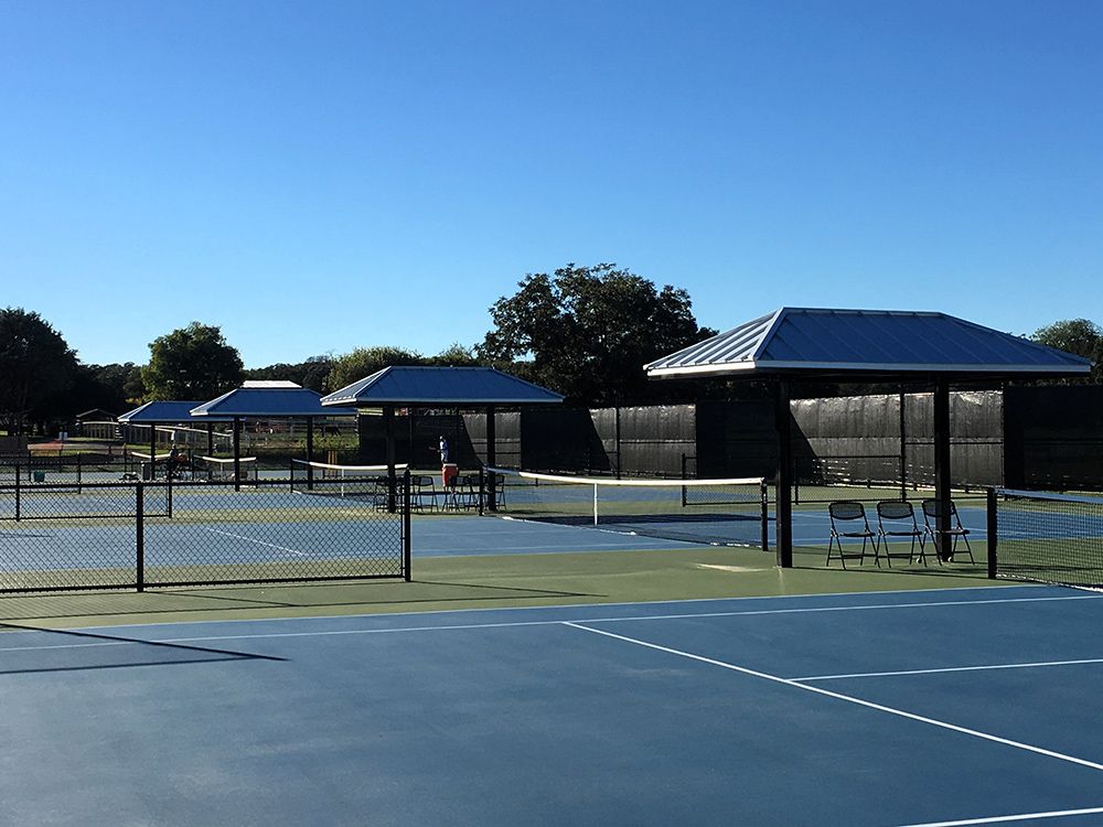 Blue tennis courts with shaded benches on a sunny day.