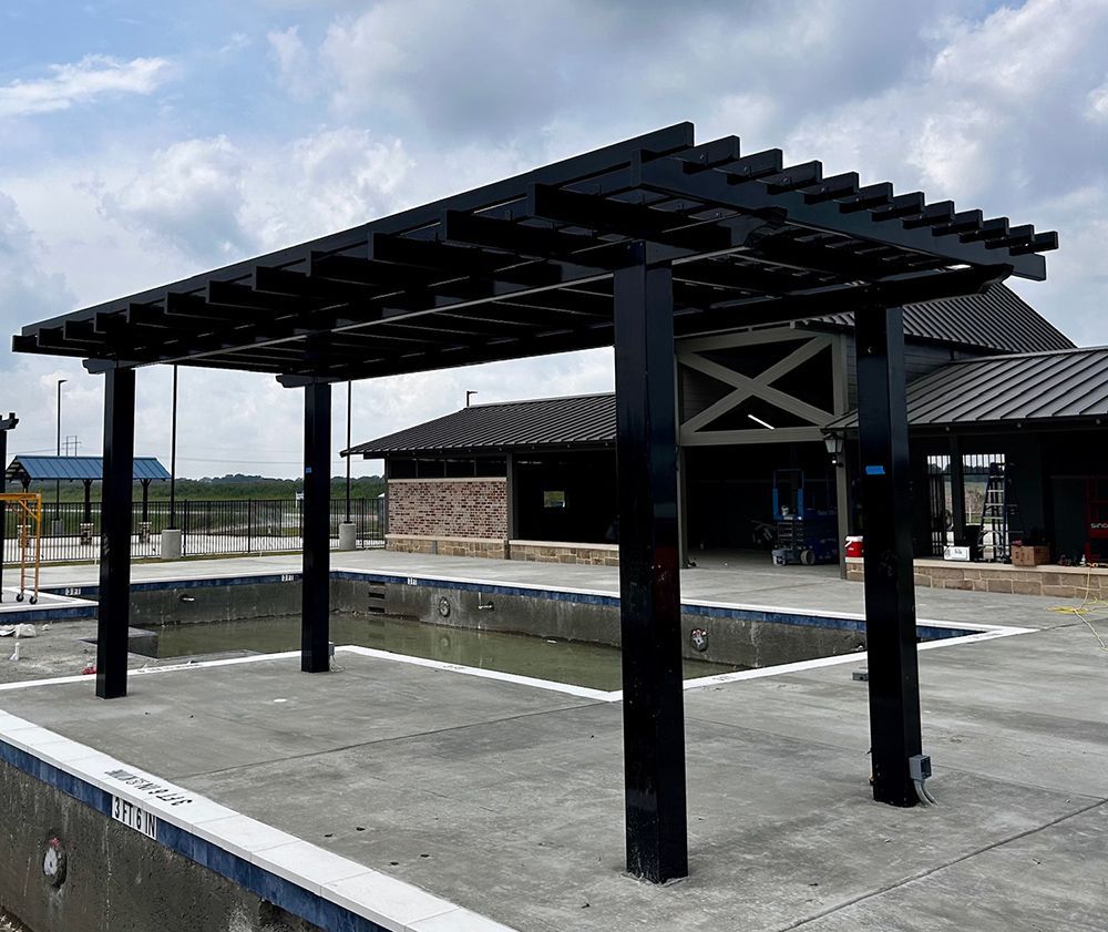Black pergola structure over an empty concrete pool. Building under construction in the background.