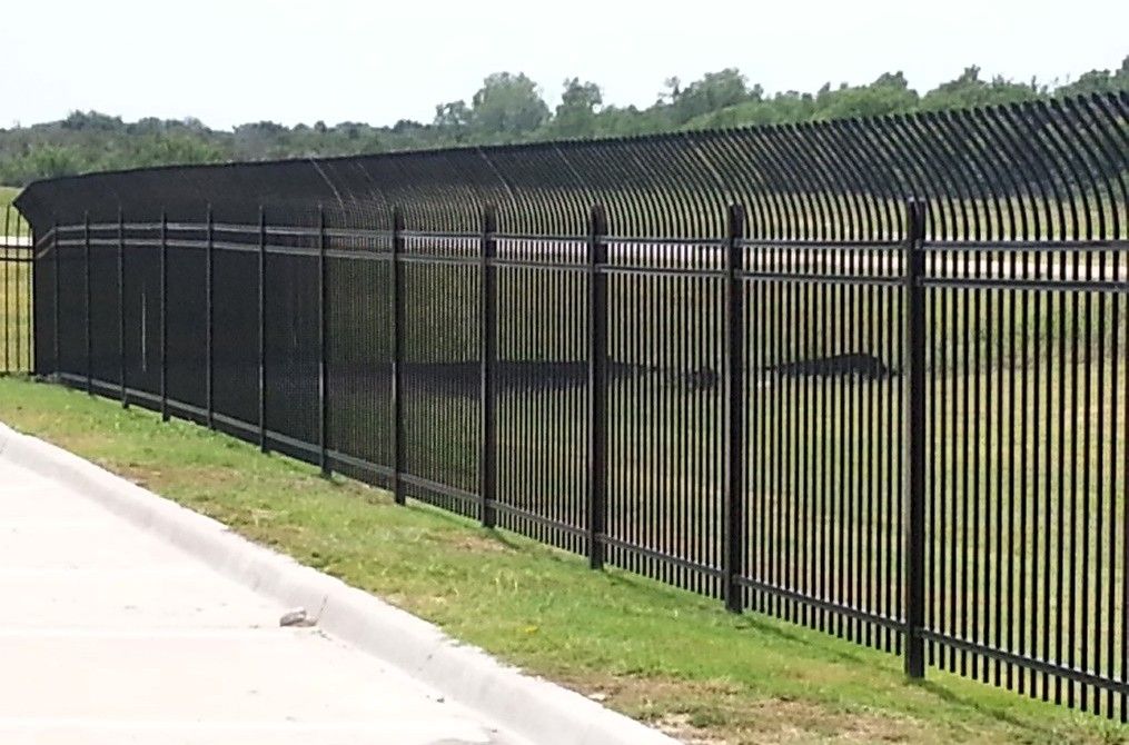 Black security fence topped with curved spikes, along green grass and a concrete curb.