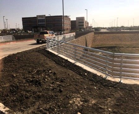 A bridge with metal railing next to a brown, muddy area with a building in the background.