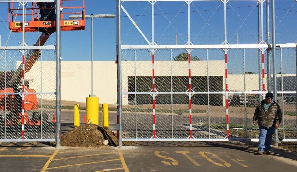 Gate with red and white poles, open for access. Man in camo jacket watches. Lift in use.