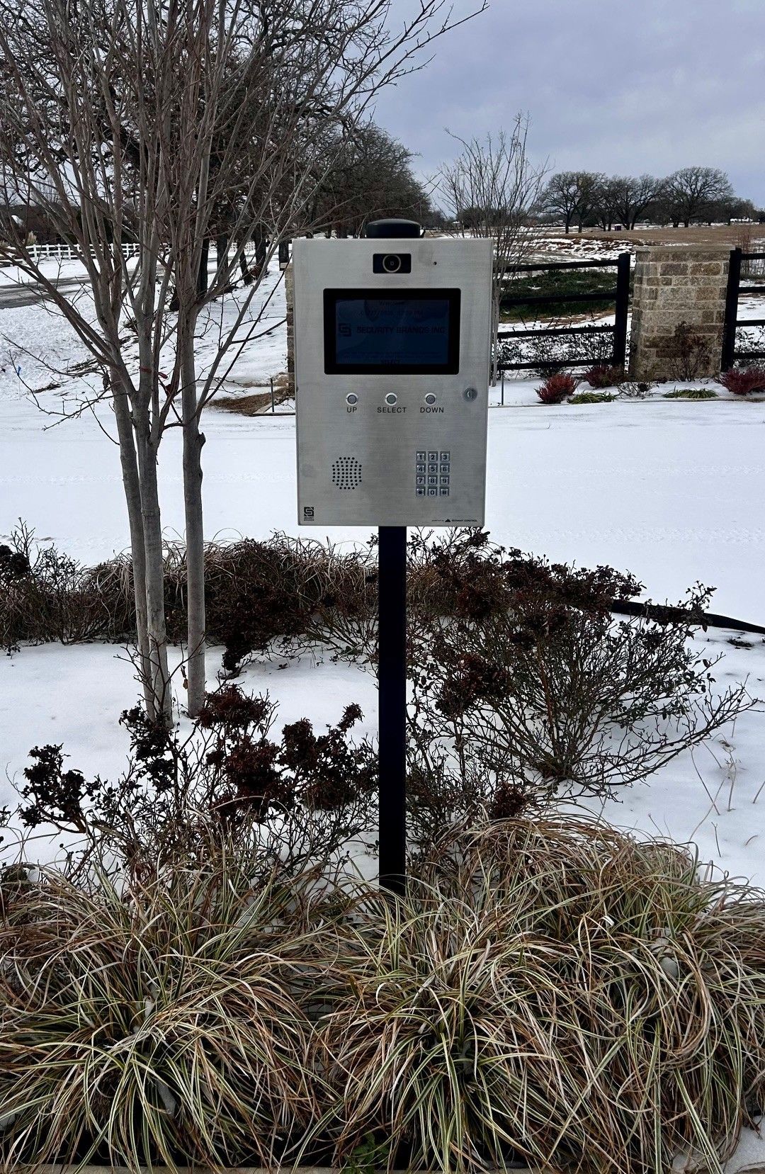 Silver intercom on post in snowy landscape, with screen and buttons.