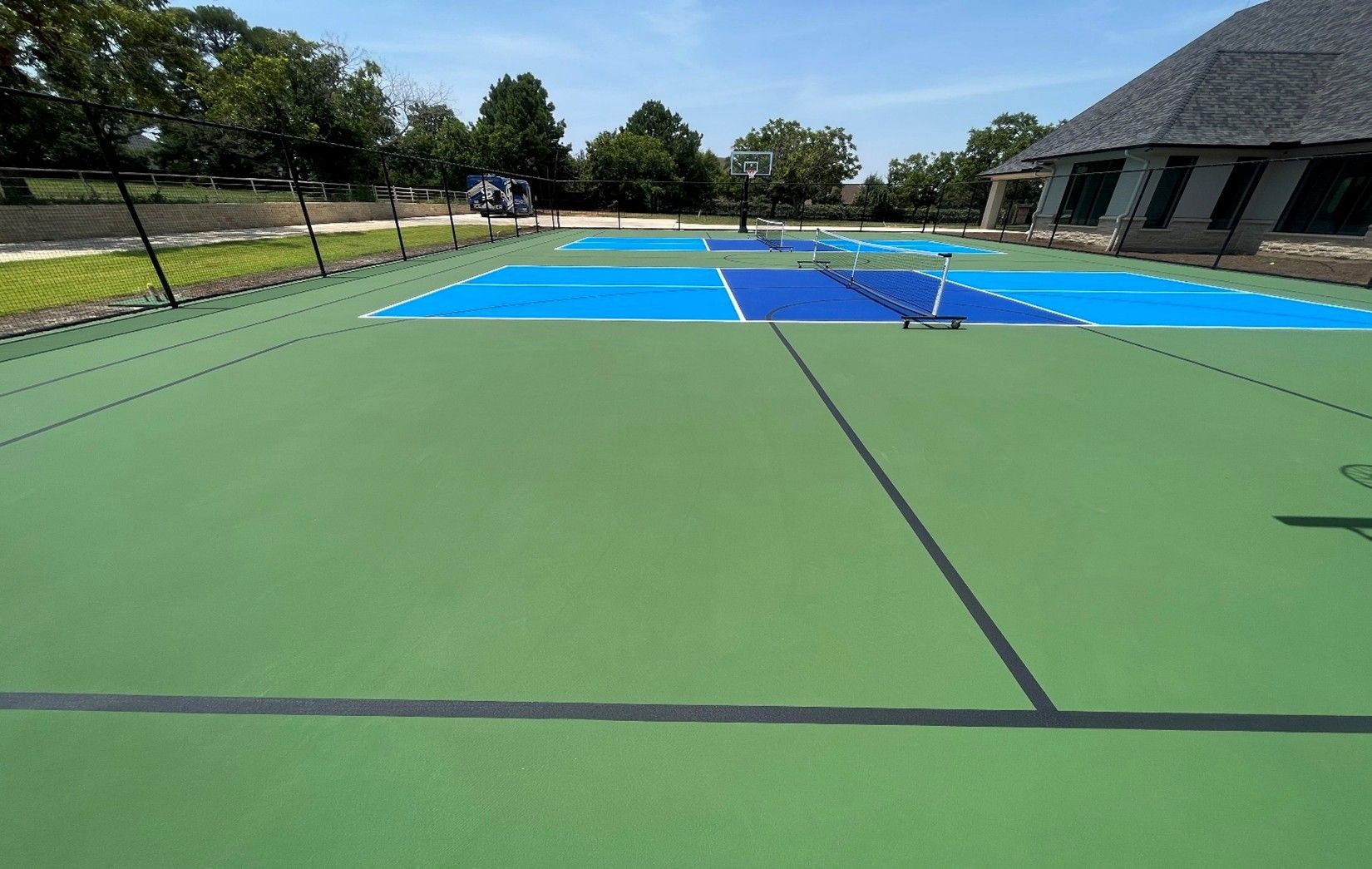 Green and blue pickleball court on a sunny day with a building in the background.