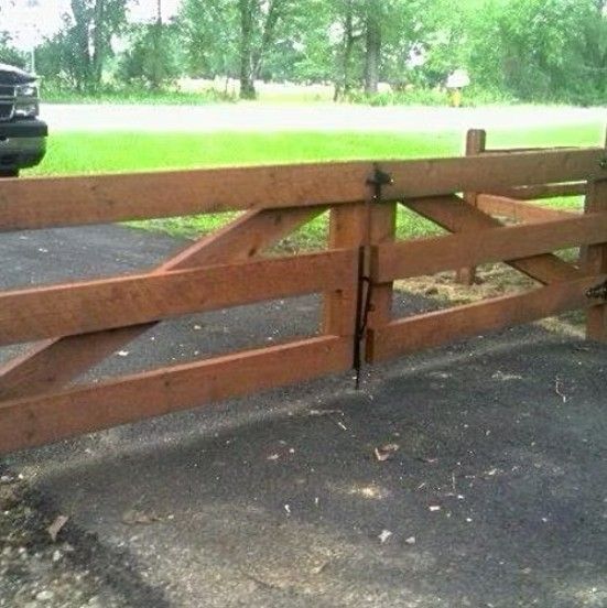 Wooden gate, brown, across a paved driveway. Green grass and a truck are in the background.