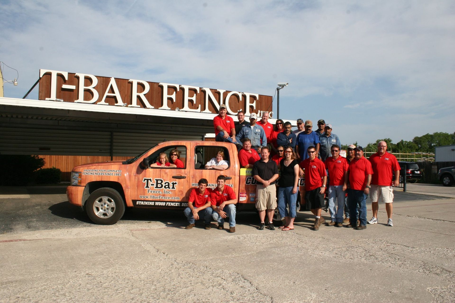 White picket fence in front of a house, with scalloped top and vertical slats.