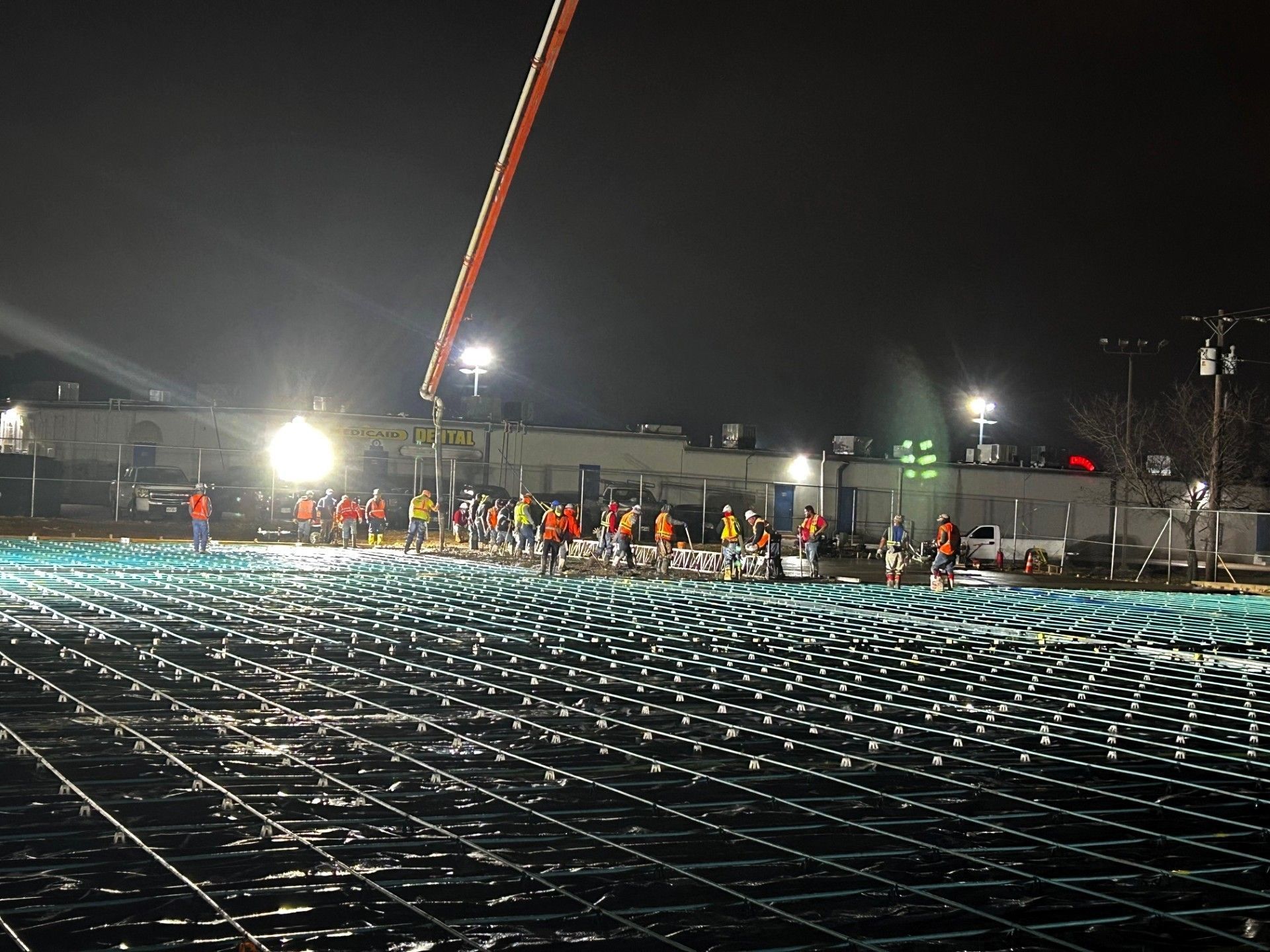 Construction site at night with workers, concrete being poured, and grid of rebar.