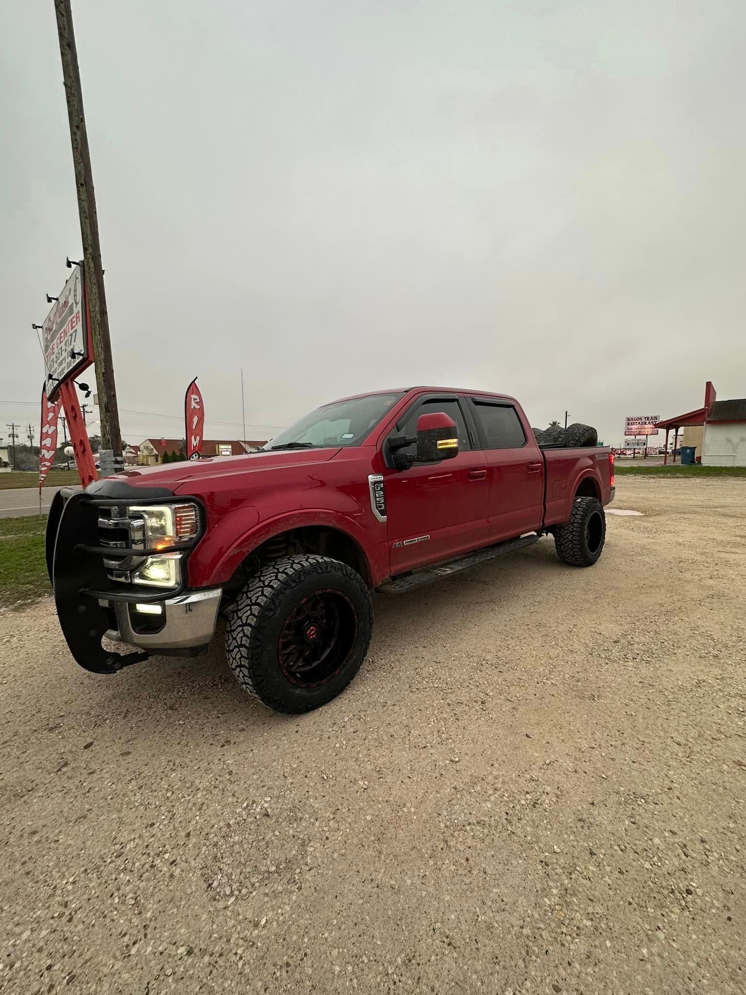 A red truck is parked in a gravel lot