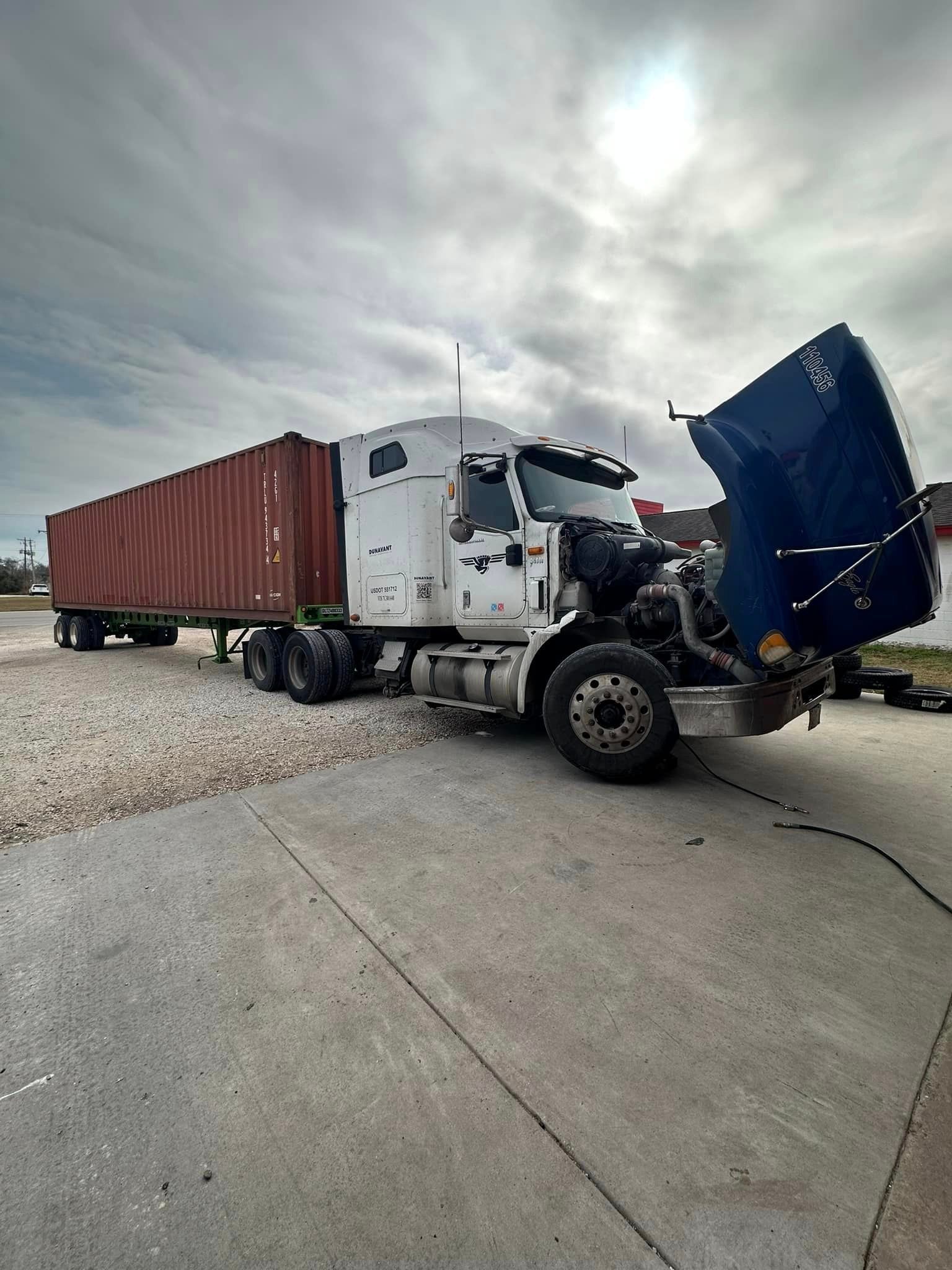A semi truck with its hood open is parked in a parking lot
