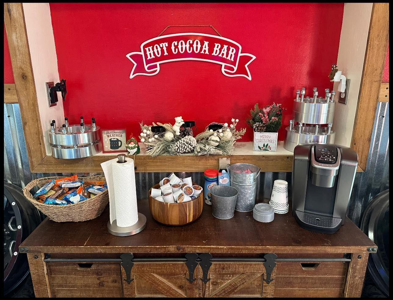 A hot cocoa bar with a sign on the wall and a coffee maker