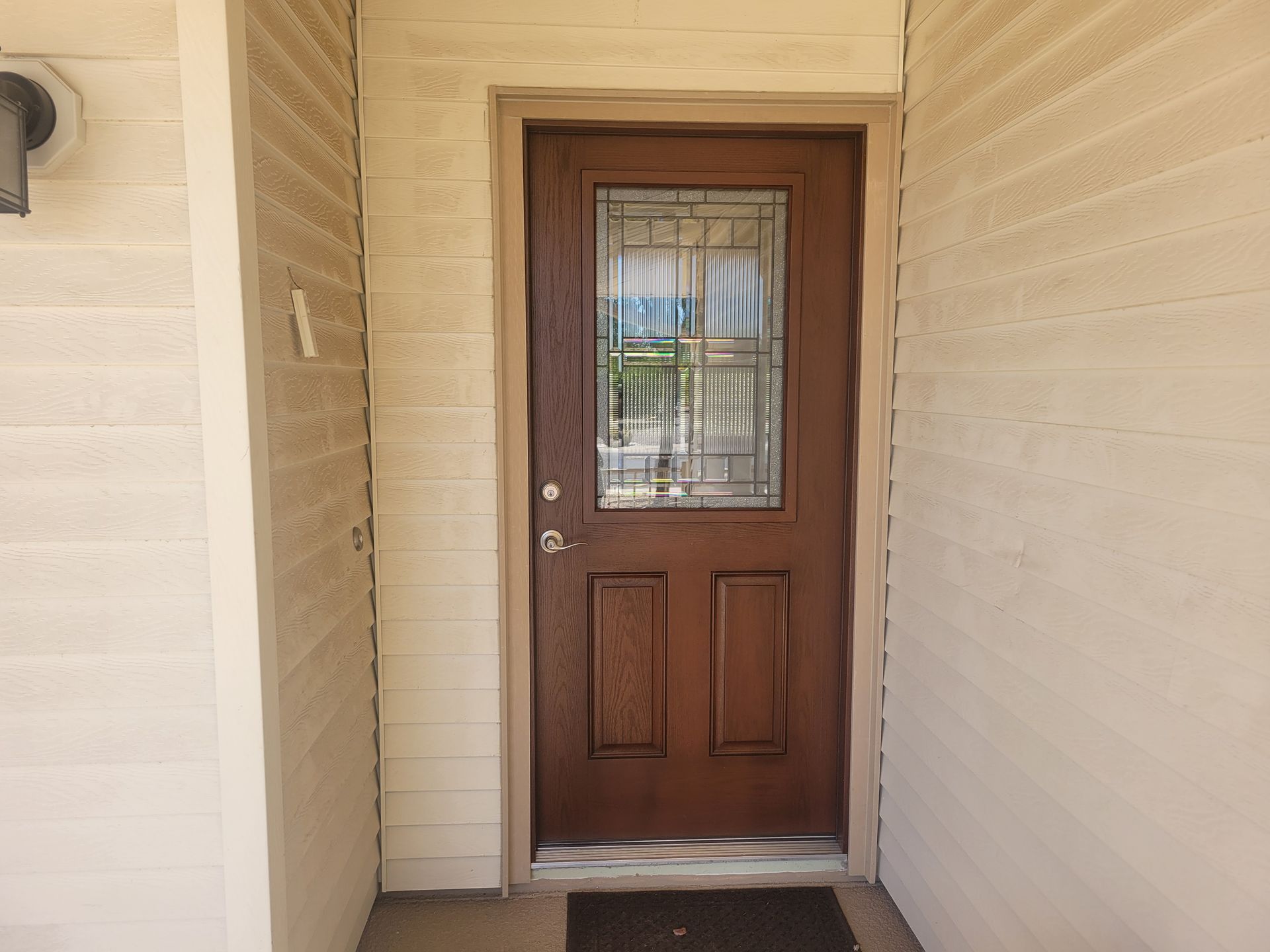 A brown door with a stained glass window is on a white wall