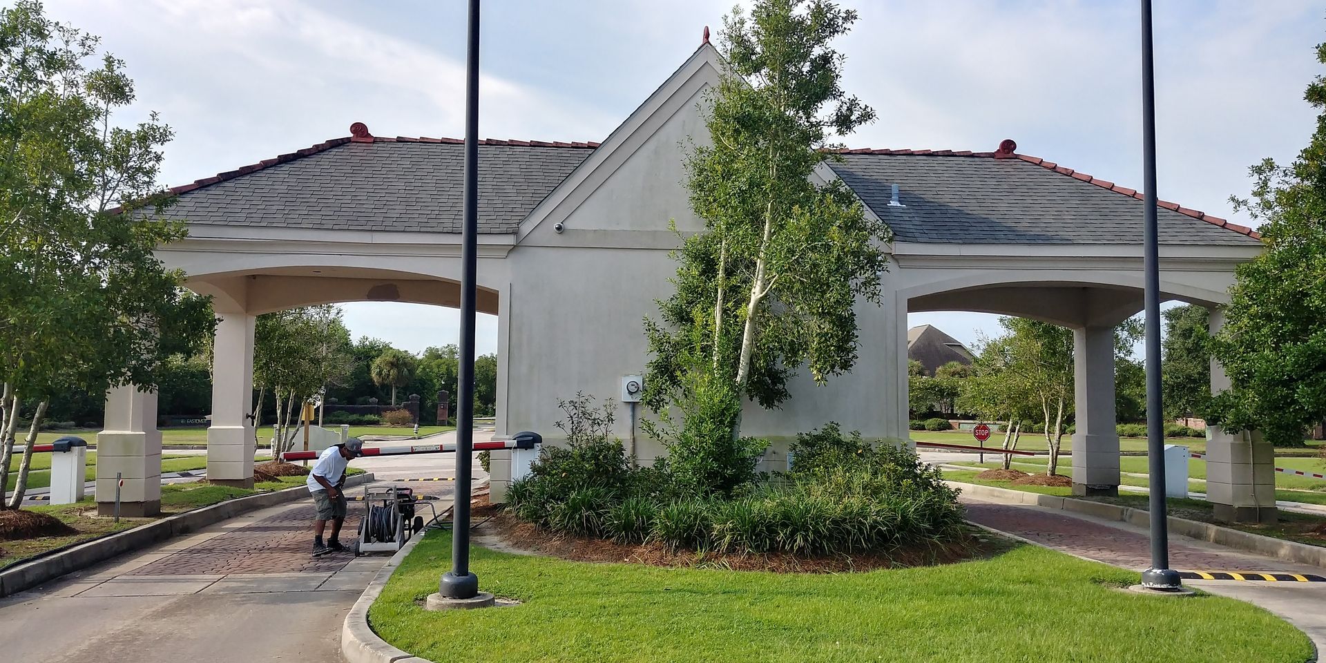 Entrance gate to a residential community with a worker operating a machine. The gate is made of white stucco with a dark roof.