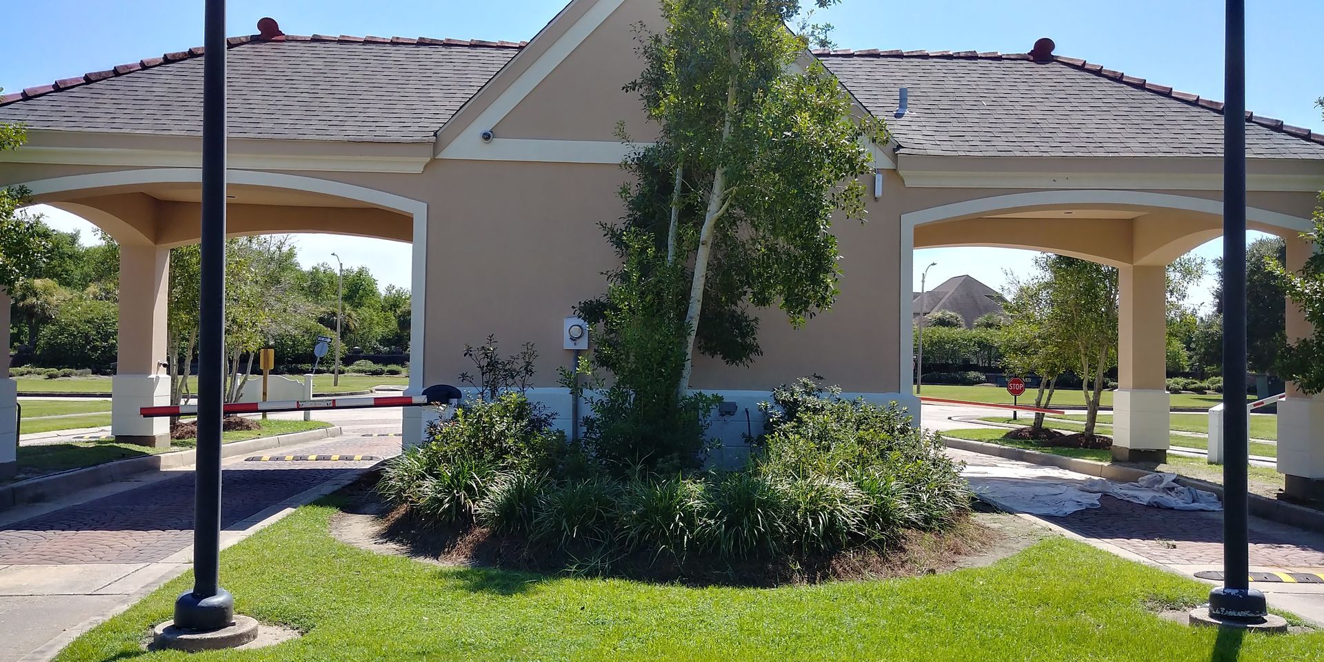 Entrance to a gated community with a beige building, arched entryways, and a small tree in the center.