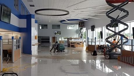 Workers inside a large, mostly empty building, likely under construction or renovation. Blue and gray walls, glossy floors, and a scissor lift are visible.