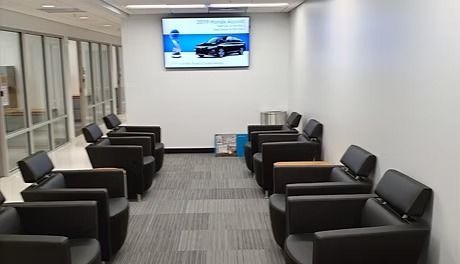 Waiting area with rows of black armchairs, gray carpet, and a TV screen on the wall.