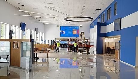 Interior view of a modern building under construction. Workers are installing a large screen; blue and white walls, wood accents, and shiny floors.