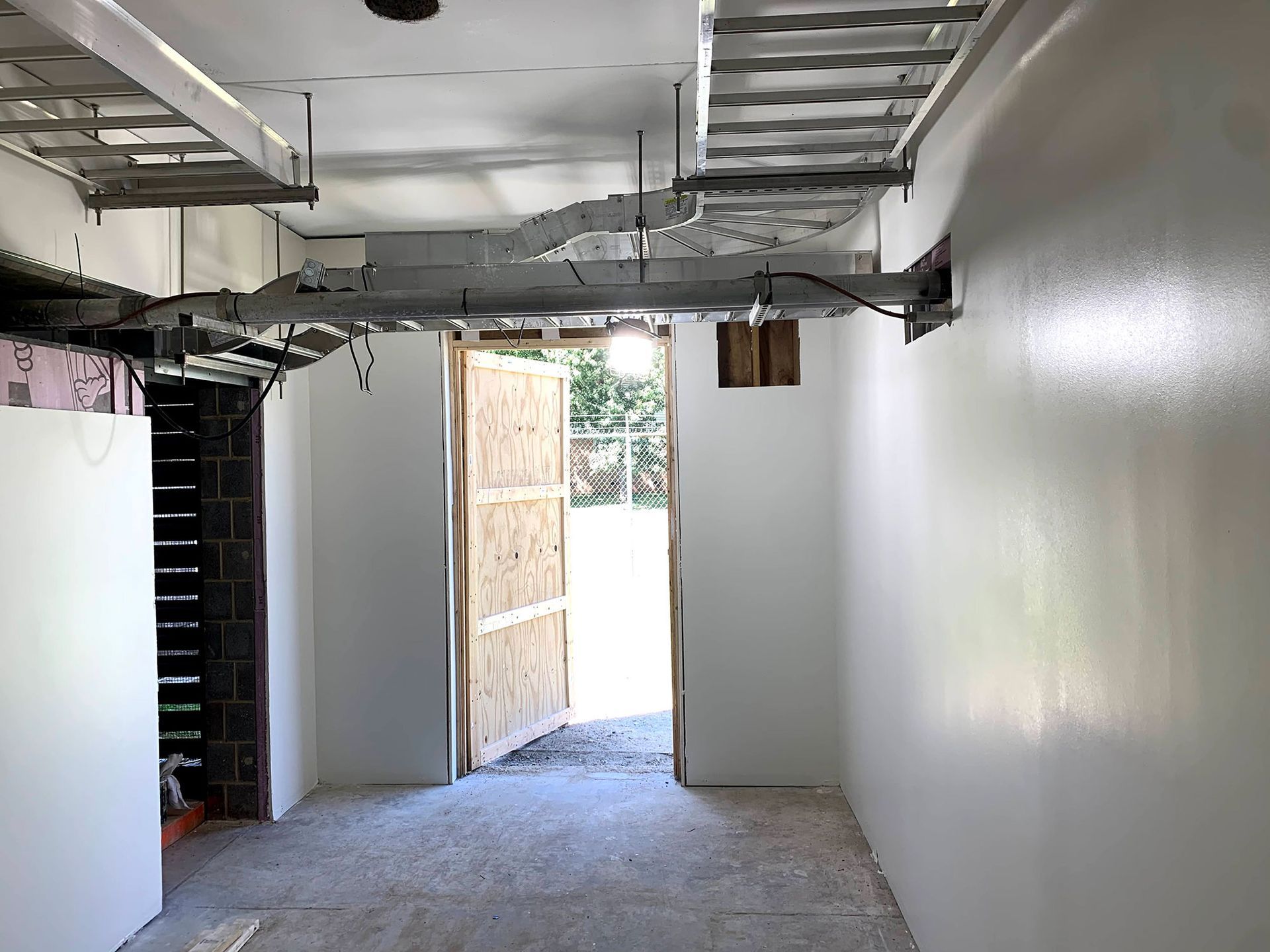 Interior view of a room under construction, with white walls, a doorway leading outside, and exposed ceiling beams.