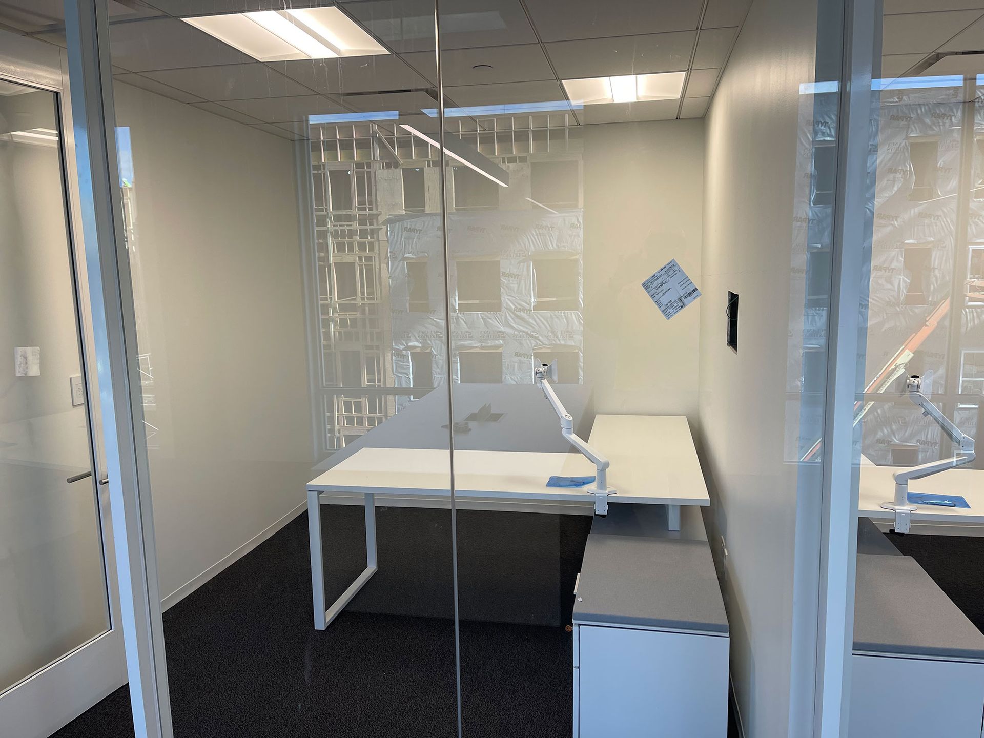 An office cubicle with white walls, a desk, and a partially visible open glass door. A blue and gray diamond shape hangs on the wall.