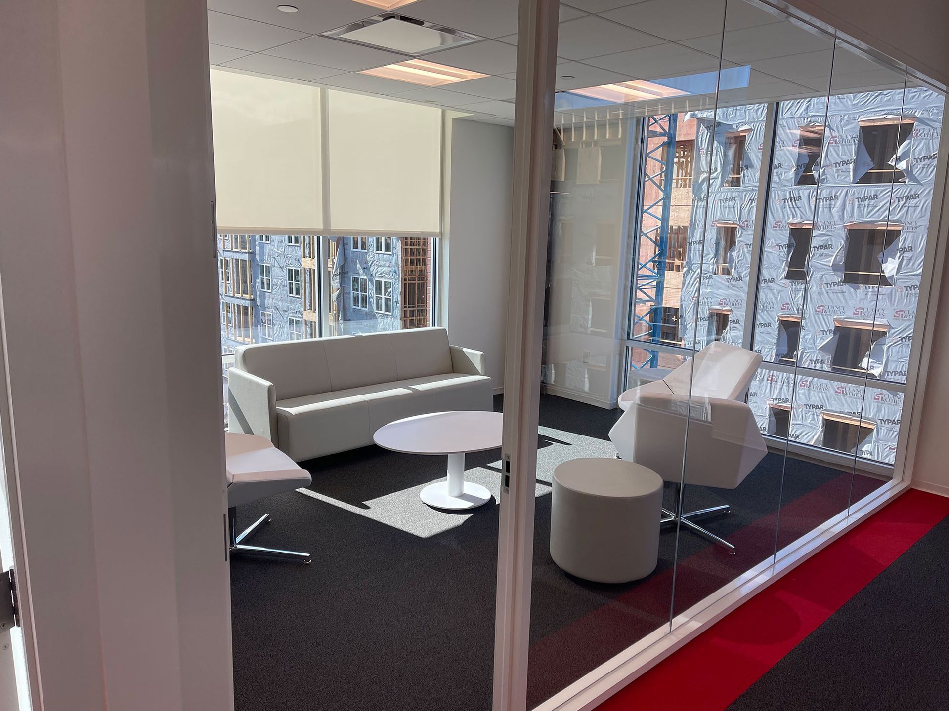 Modern office waiting area with white furniture, a small round table, and a large window with a city view.