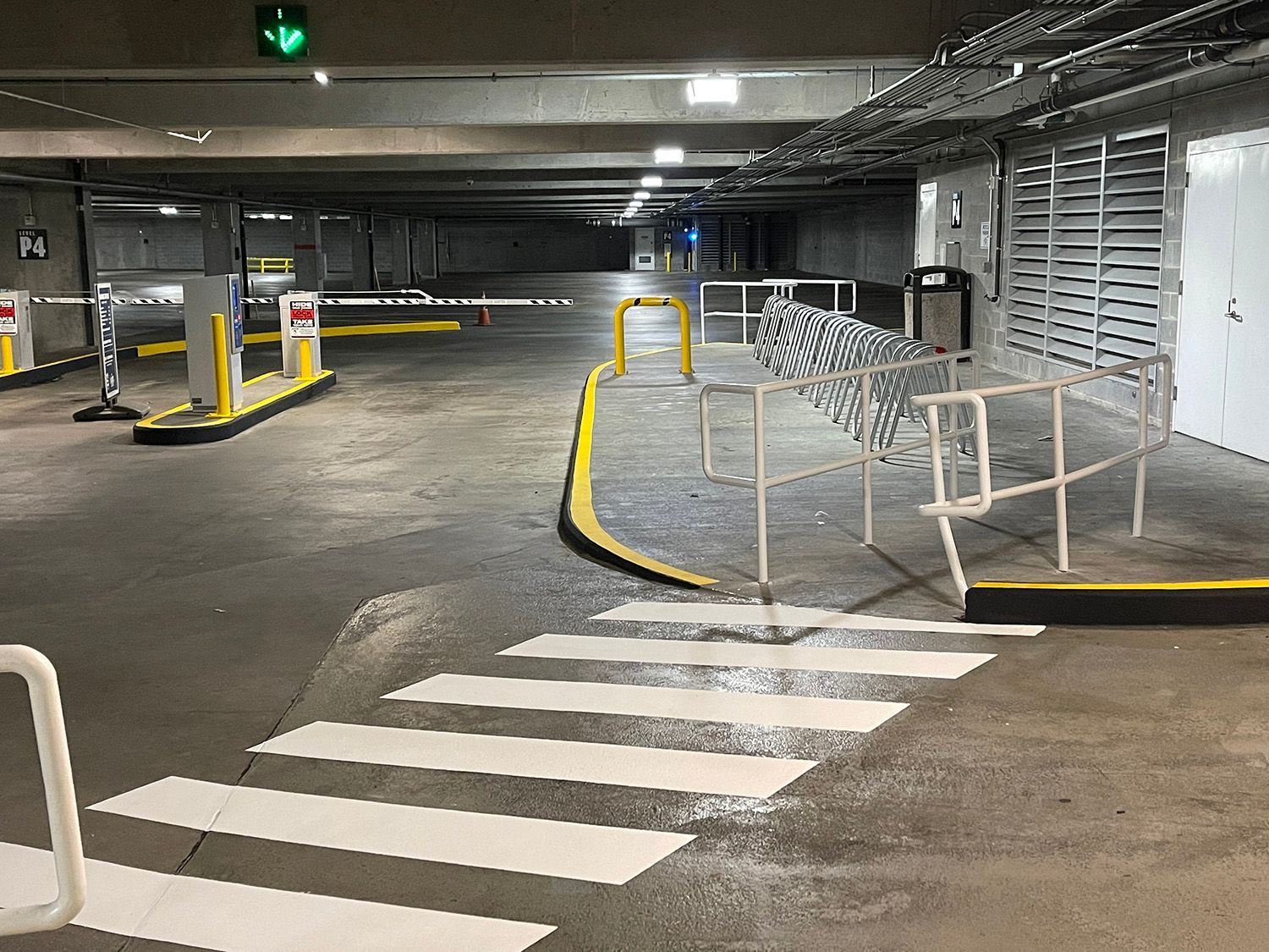 Crosswalk and pedestrian railing in a parking garage, leading toward barriers and an exit.