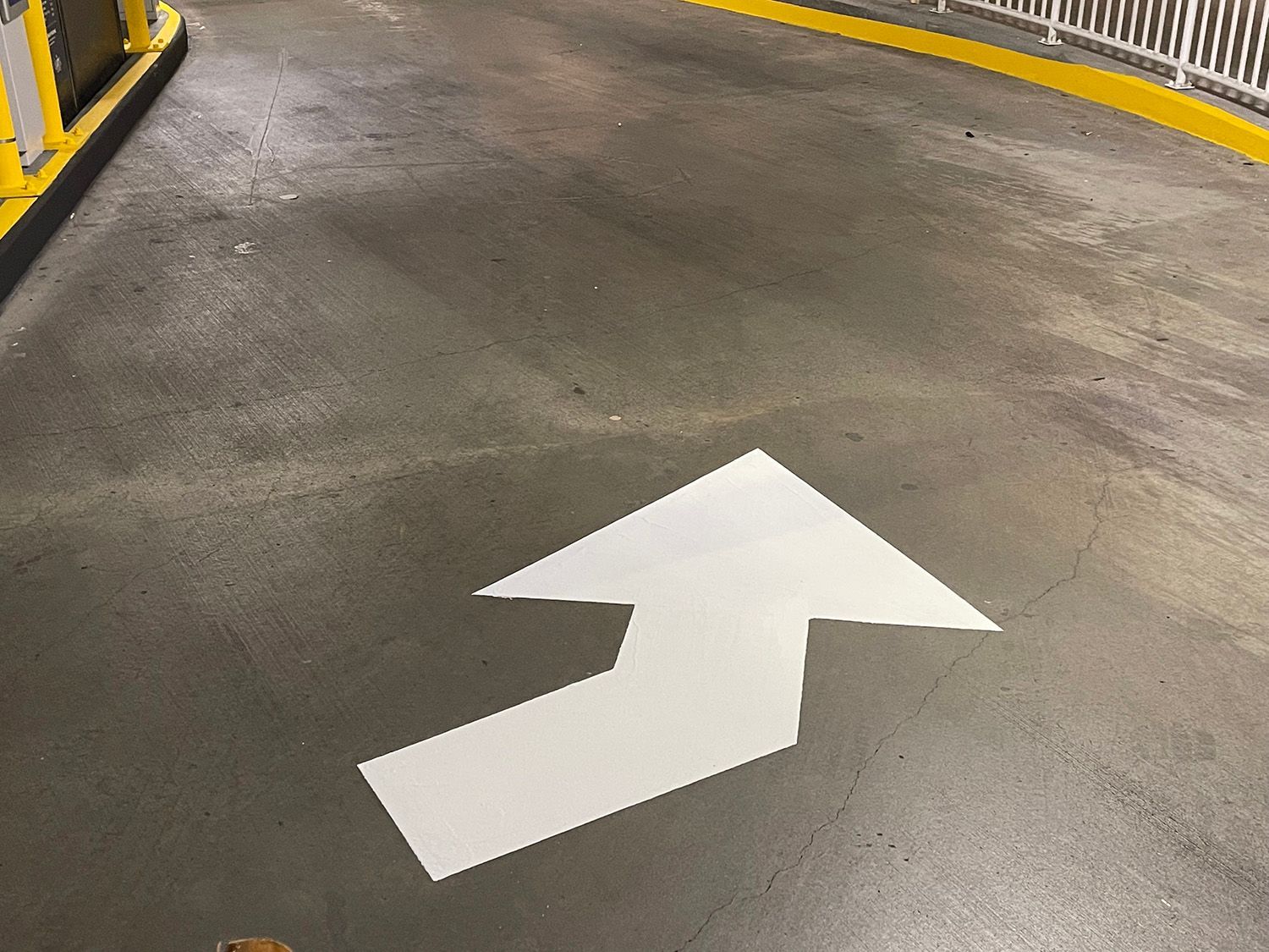 White arrow painted on gray asphalt, indicating direction of travel, possibly in a parking structure.