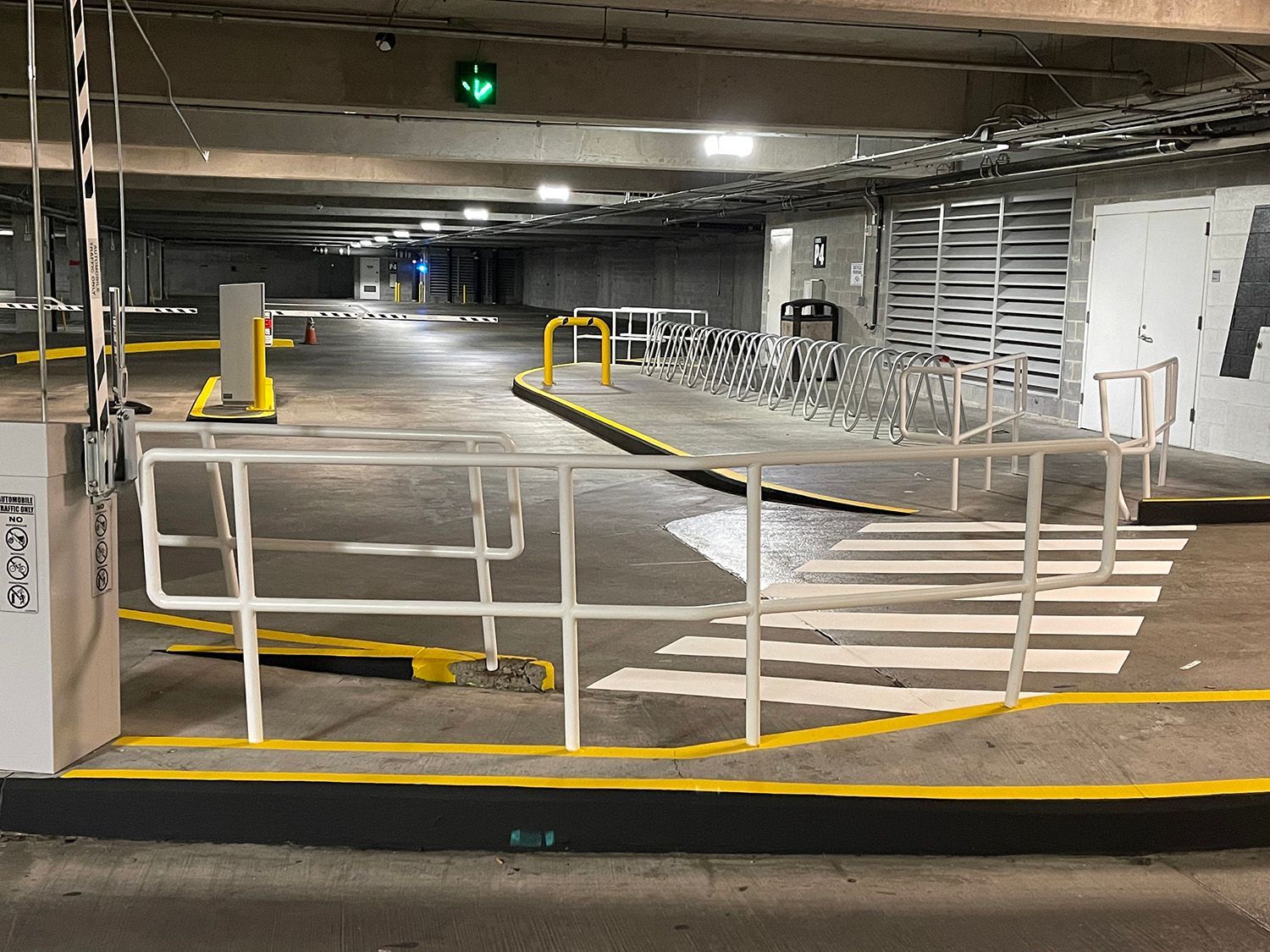 Underground parking garage entrance with a barrier gate, crosswalk, and green light. Grey concrete setting with yellow and white painted lines.