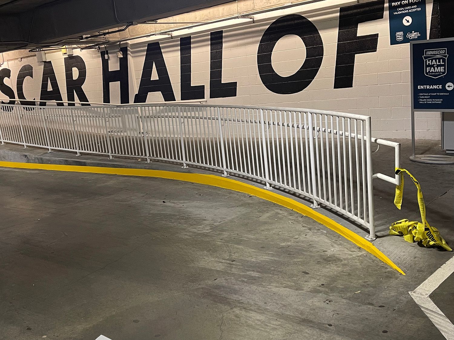 A parking garage with a white railing along a yellow curb. Large black text on the wall reads 
