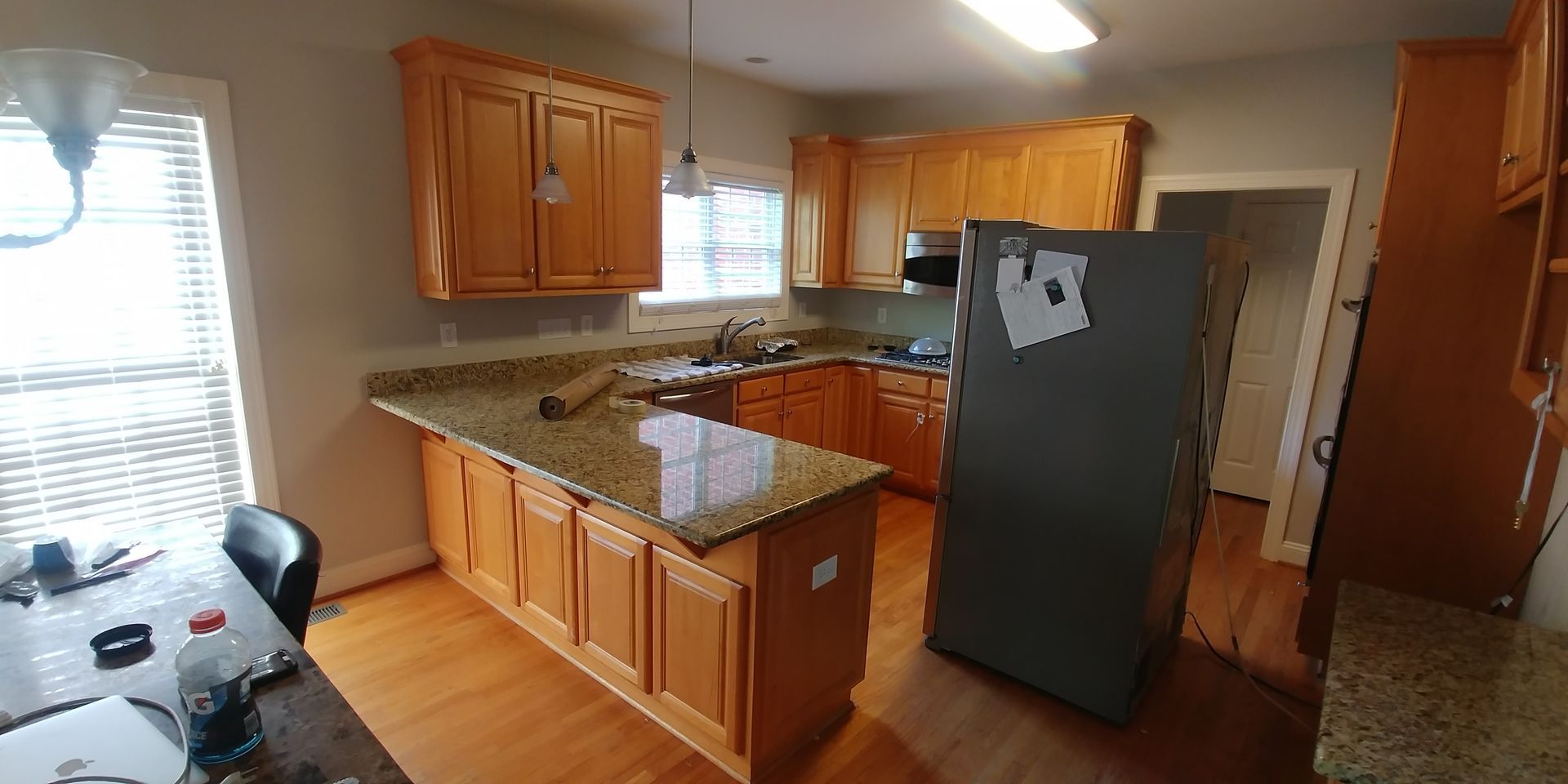 Kitchen with wooden cabinets, granite countertops, and a stainless steel refrigerator. The room has a window with blinds.
