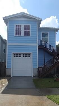 Two-story light blue house with white garage door, two windows on second floor, and exterior staircase.