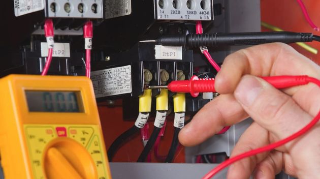 Technician testing electrical panel with a multimeter and red probe wires