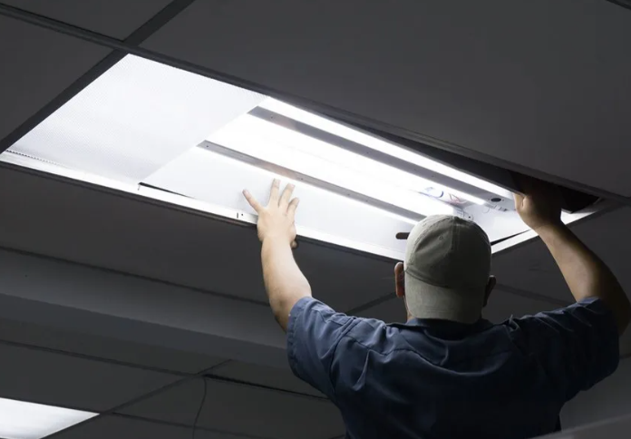 Technician replacing a fluorescent ceiling light panel in an office ceiling