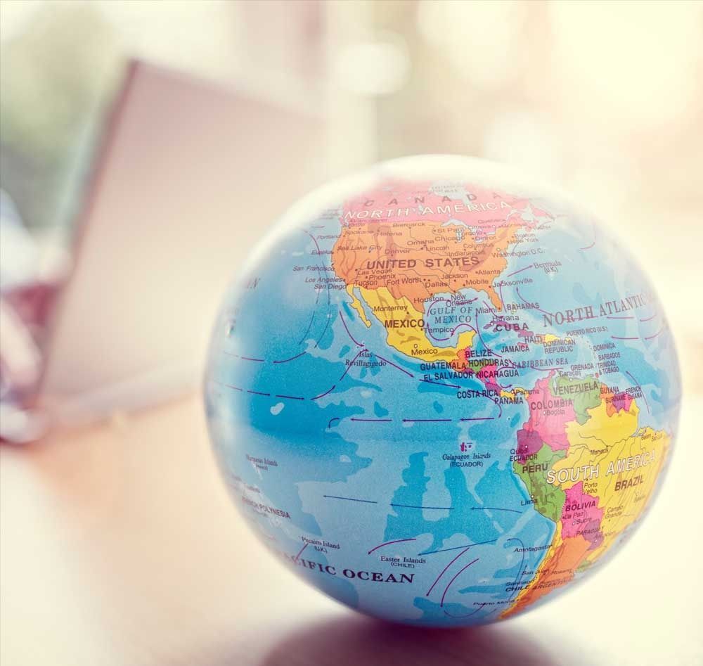 A colorful globe sits on a wooden surface, with a blurred background suggesting a laptop.