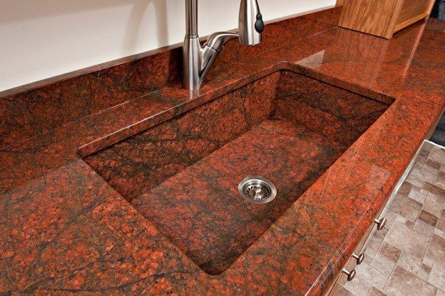 A kitchen sink with a red granite counter top and a faucet.
